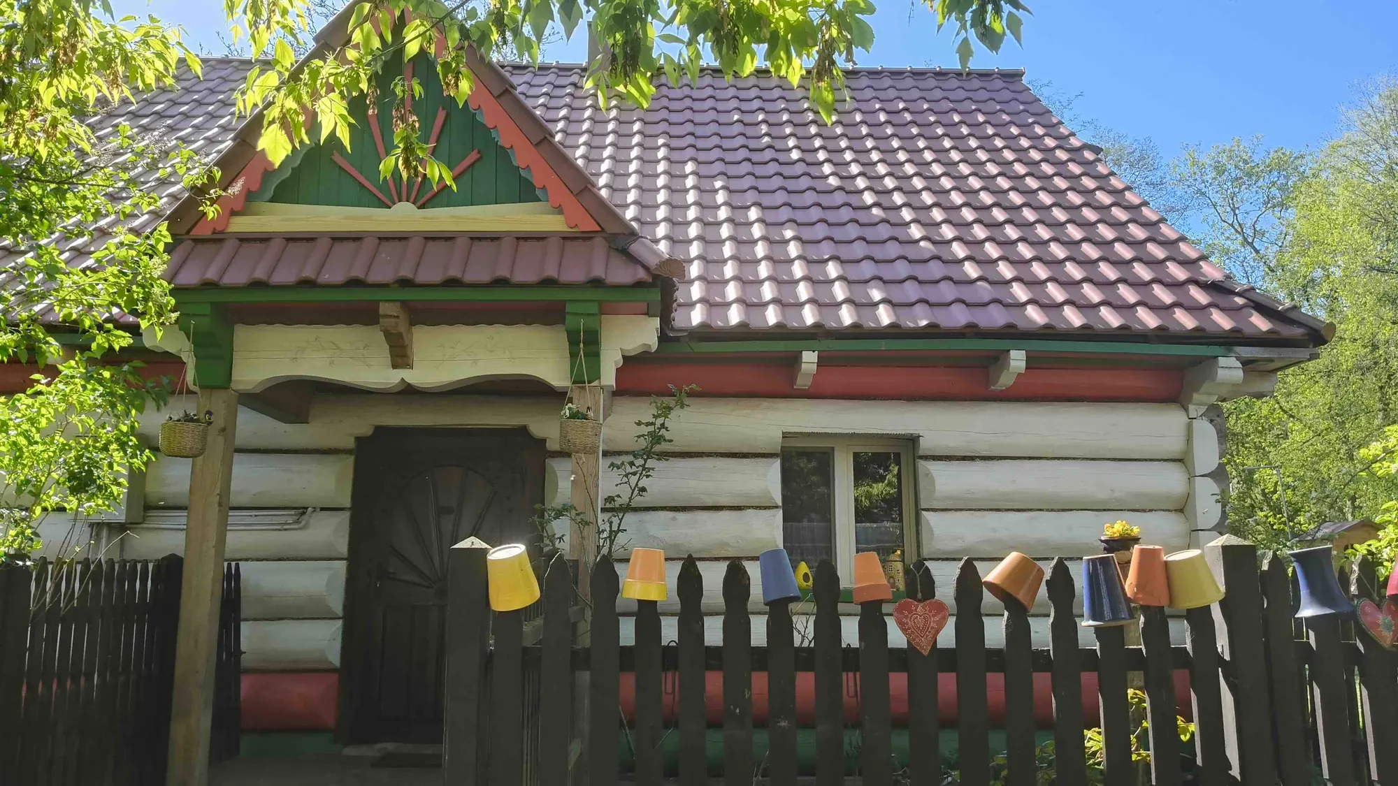 Chałupa Basieńki: bielone bale, zielono-czerwony ganek i płot z doniczkami